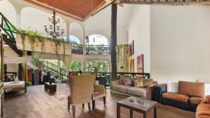 Un vaste espace de vie doté d’un plancher en bois, d’un canapé, d’un fauteuil et d’une table basse. On y trouve un escalier avec une rampe et des plantes suspendues au plafond.