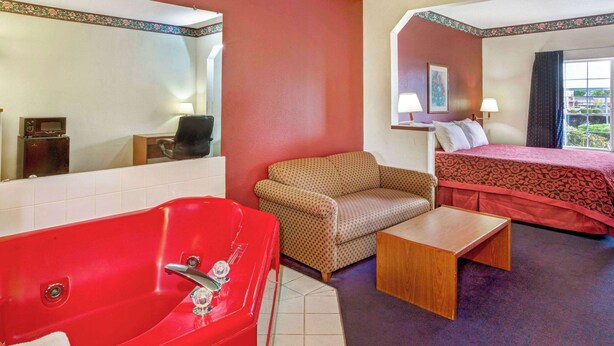 Habitación de hotel con una bañera roja, un sofá, una cama con colcha roja, una mesita de madera y una ventana con vistas.