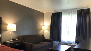 Una habitación de hotel con una cama, un escritorio con lámpara, un sofá, una mesita y una silla.