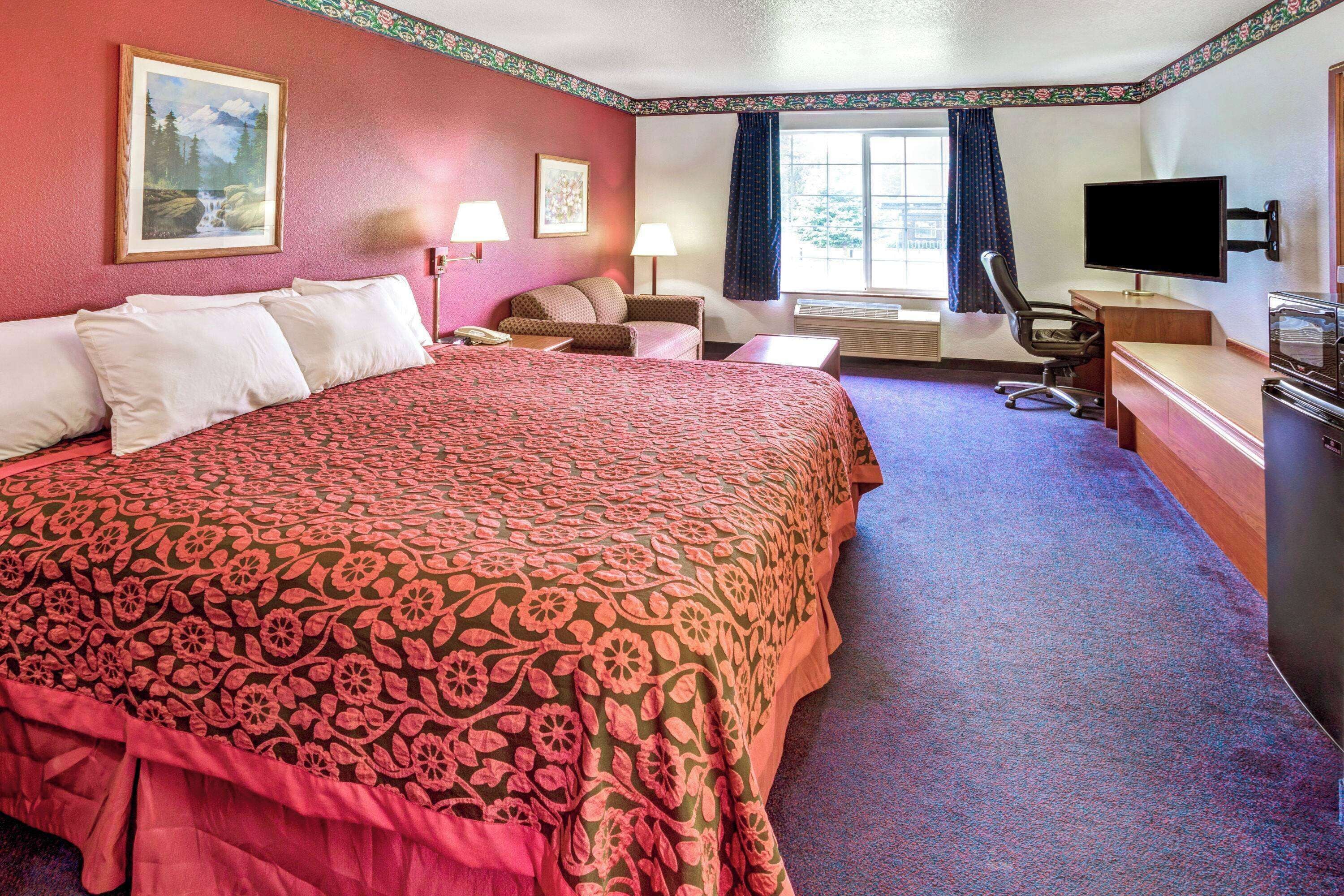 A hotel room with a large bed, a desk with a computer, a TV, and a window with curtains.