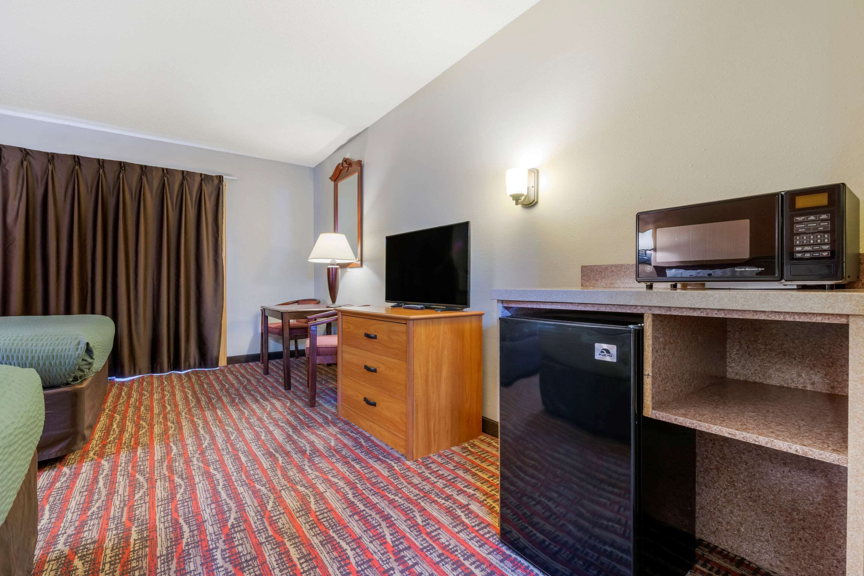 Habitació d'hotel amb llit, escriptori amb làmpada, televisió, microones i nevera.