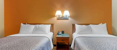A hotel room with two beds, a nightstand with a lamp, and a patterned carpet.