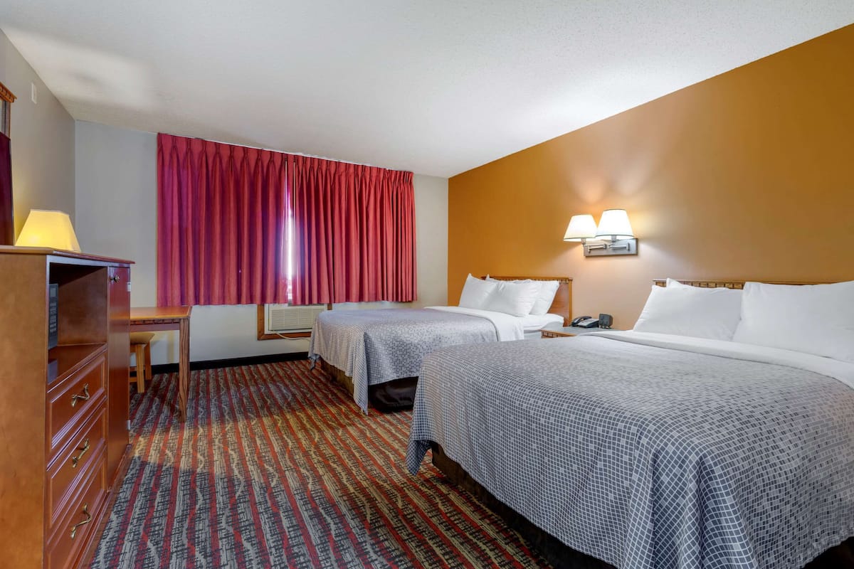 A hotel room with two beds, a desk, a dresser, and a large window with curtains.