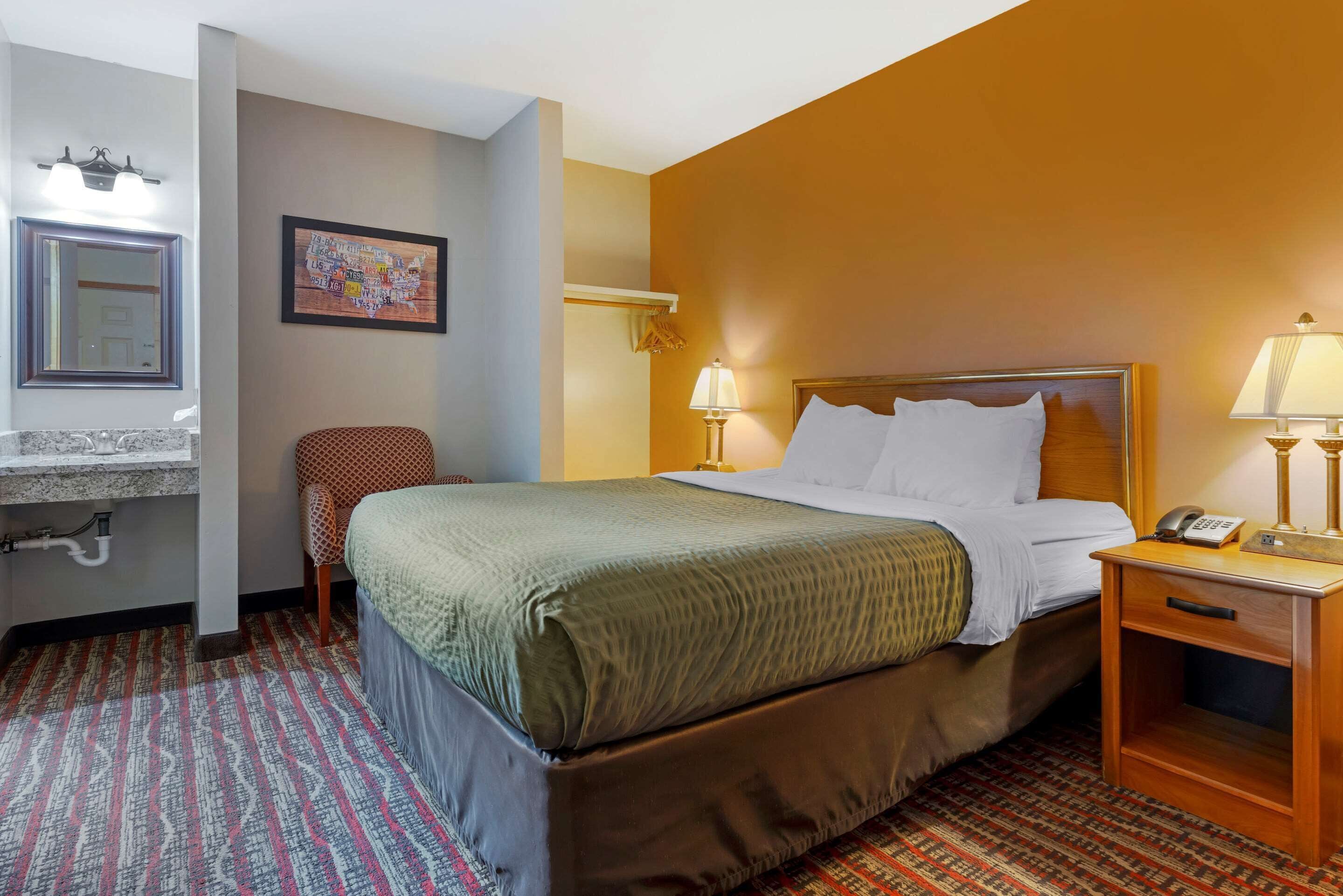 A hotel room with a bed, bedside table, lamp, and a chair.