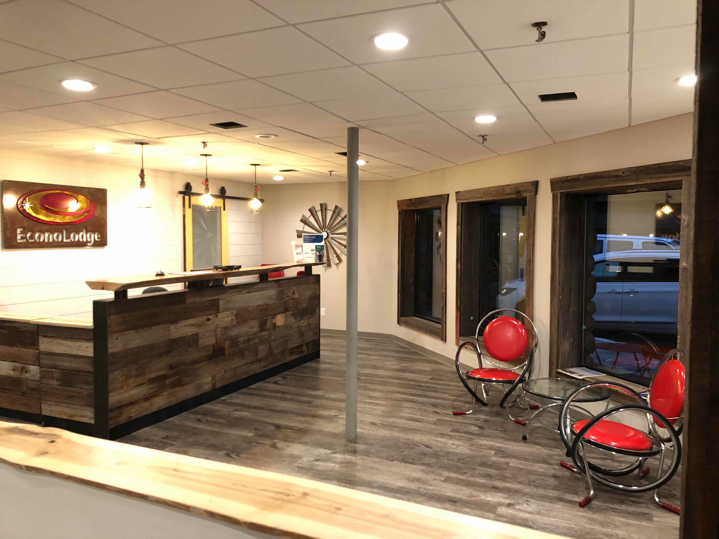 A reception area with a wooden reception desk, two red chairs, and a clock on the wall.