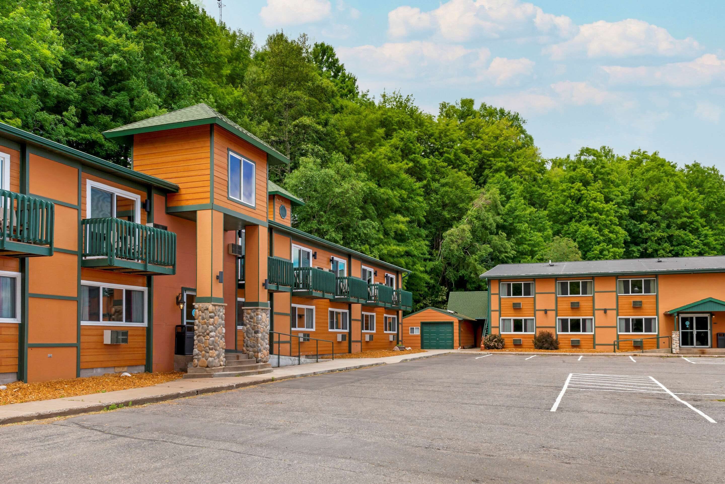 A multi-story motel with balconies, a parking lot, and a forested backdrop.