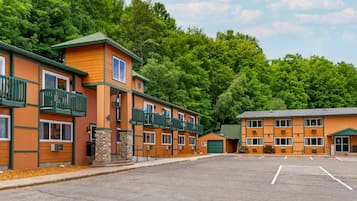 A multi-story motel with balconies, a parking lot, and a forested backdrop.