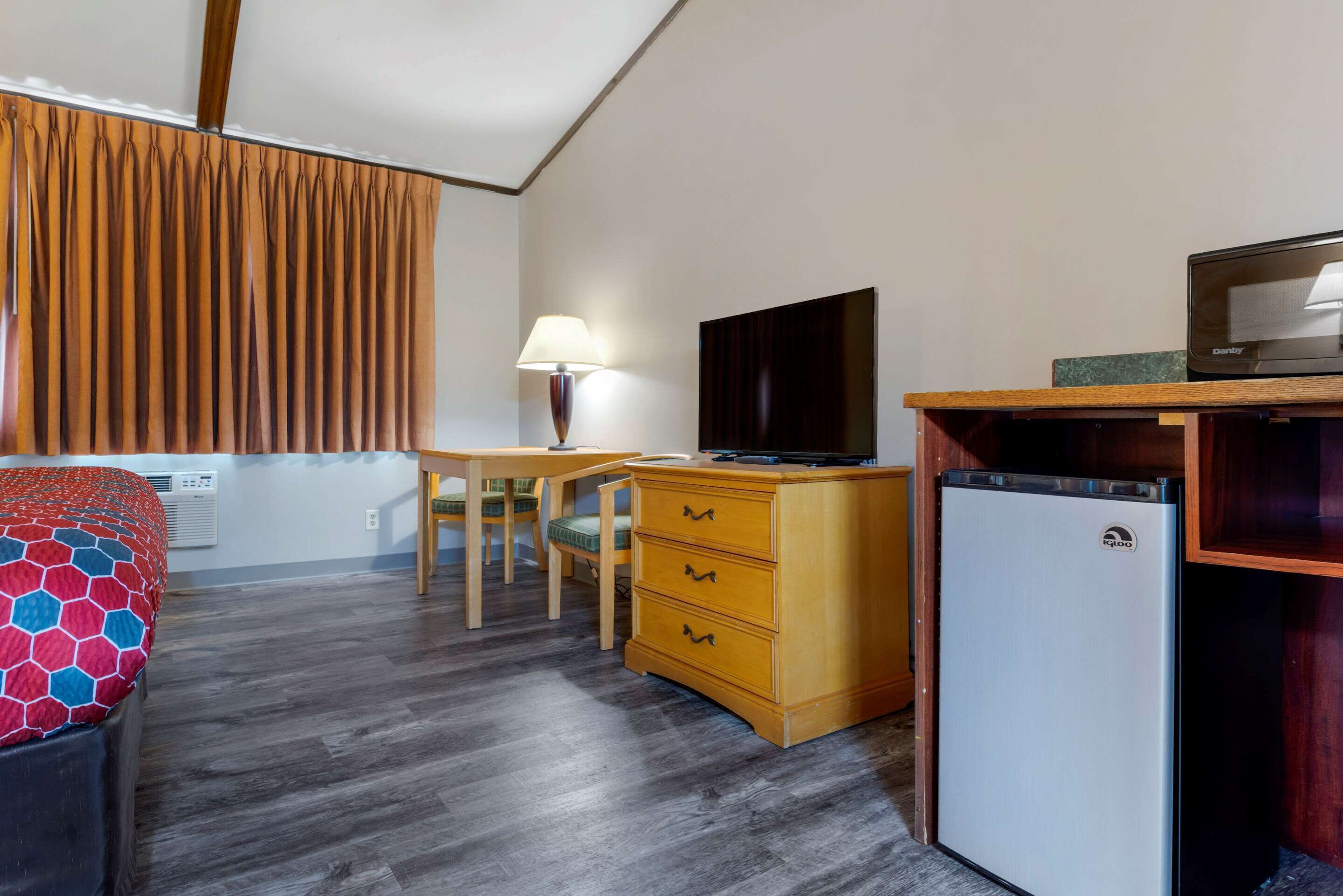 Habitación de hotel compacta con cama, escritorio, televisión, refrigerador y ventana con cortinas.