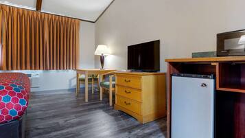 Habitación de hotel compacta con cama, escritorio, televisión, refrigerador y ventana con cortinas.