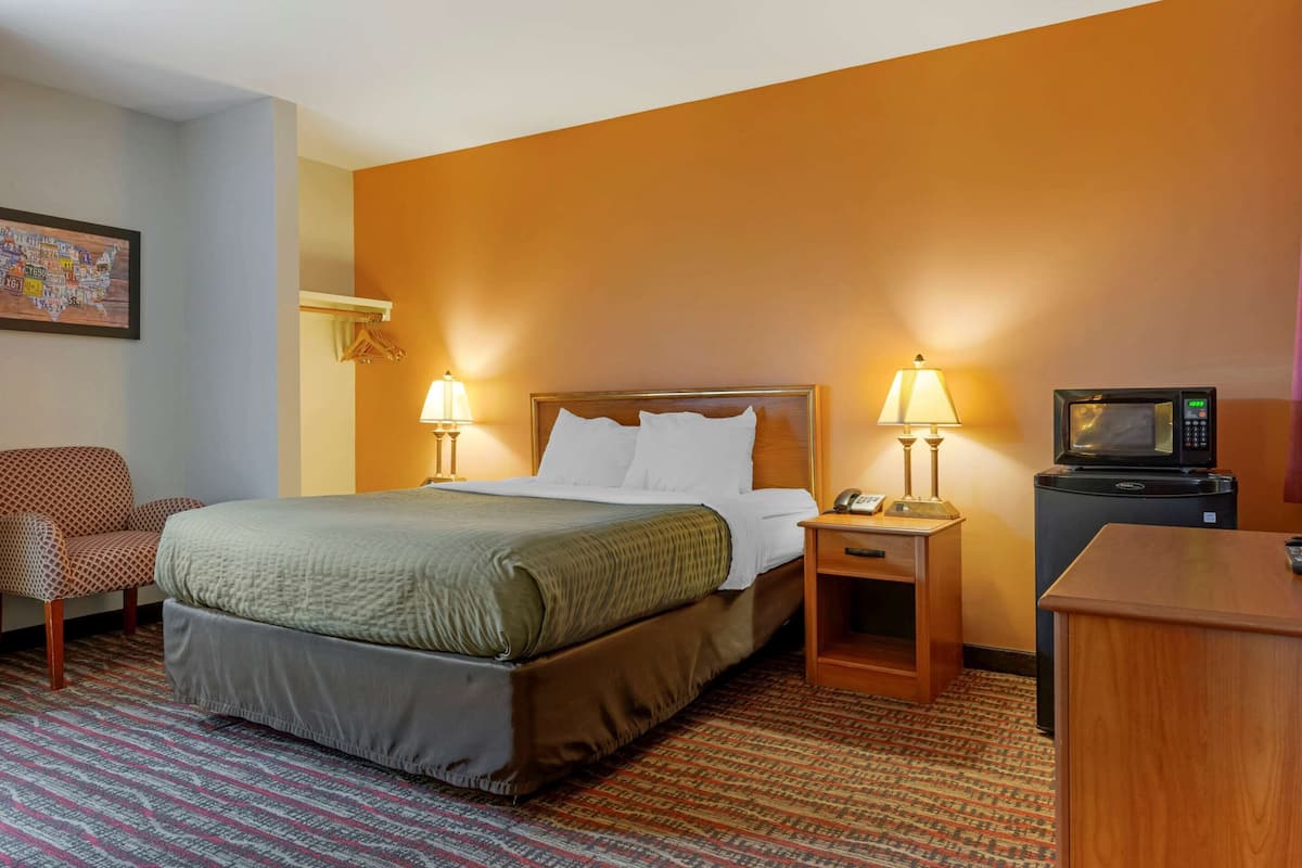 A hotel room with a bed, two bedside lamps, a television, a desk, and a chair.