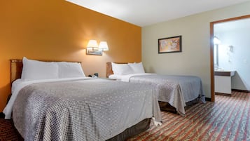 A hotel room with two beds, a patterned carpet, a wall-mounted lamp, and a framed picture.