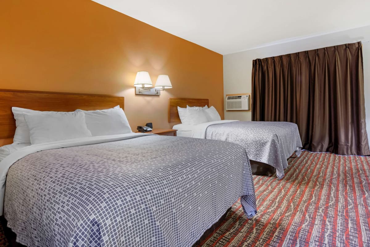 A hotel room with two beds, a wooden headboard, a nightstand with a lamp, and a patterned carpet.