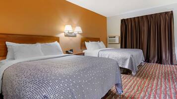 Habitación de hotel con dos camas, cabecera de madera, mesita de noche con lámpara y alfombra estampada.