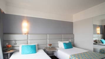 A hotel room with two beds, a small table with a vase of flowers, and a mirror on the wall.