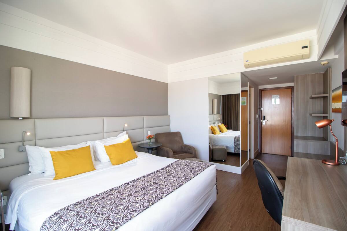 Habitación de hotel con una cama grande, un escritorio, una silla y un espejo.
