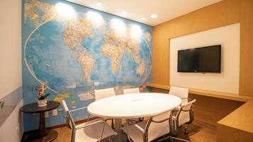 Un salón de conferencias con un gran mapa del mundo en la pared, una mesa redonda y un televisor de pantalla plana.