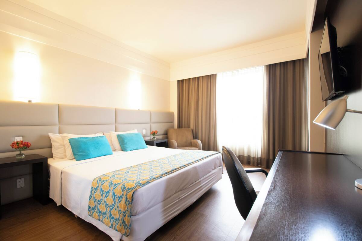 Una habitación de hotel con una cama grande, un escritorio, una silla, un televisor y cortinas.