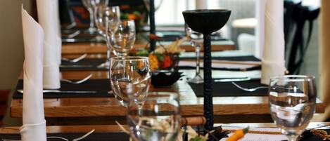 A dining table set with wine glasses, plates, and cutlery, with a view of greenery outside.