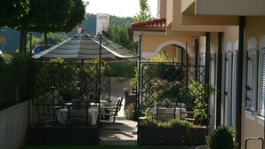 Une terrasse avec des sièges extérieurs, un parasol à rayures et, au loin, la vue sur un hôtel.