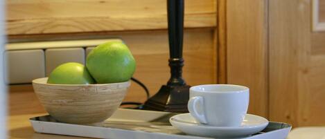 A wooden cabinet with a bowl of green apples and a white cup on a tray.