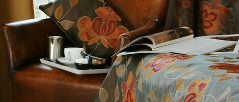 Un fauteuil en cuir agrémenté d’un coussin à motifs floraux et d’un plateau sur lequel se trouvent une tasse et une soucoupe.