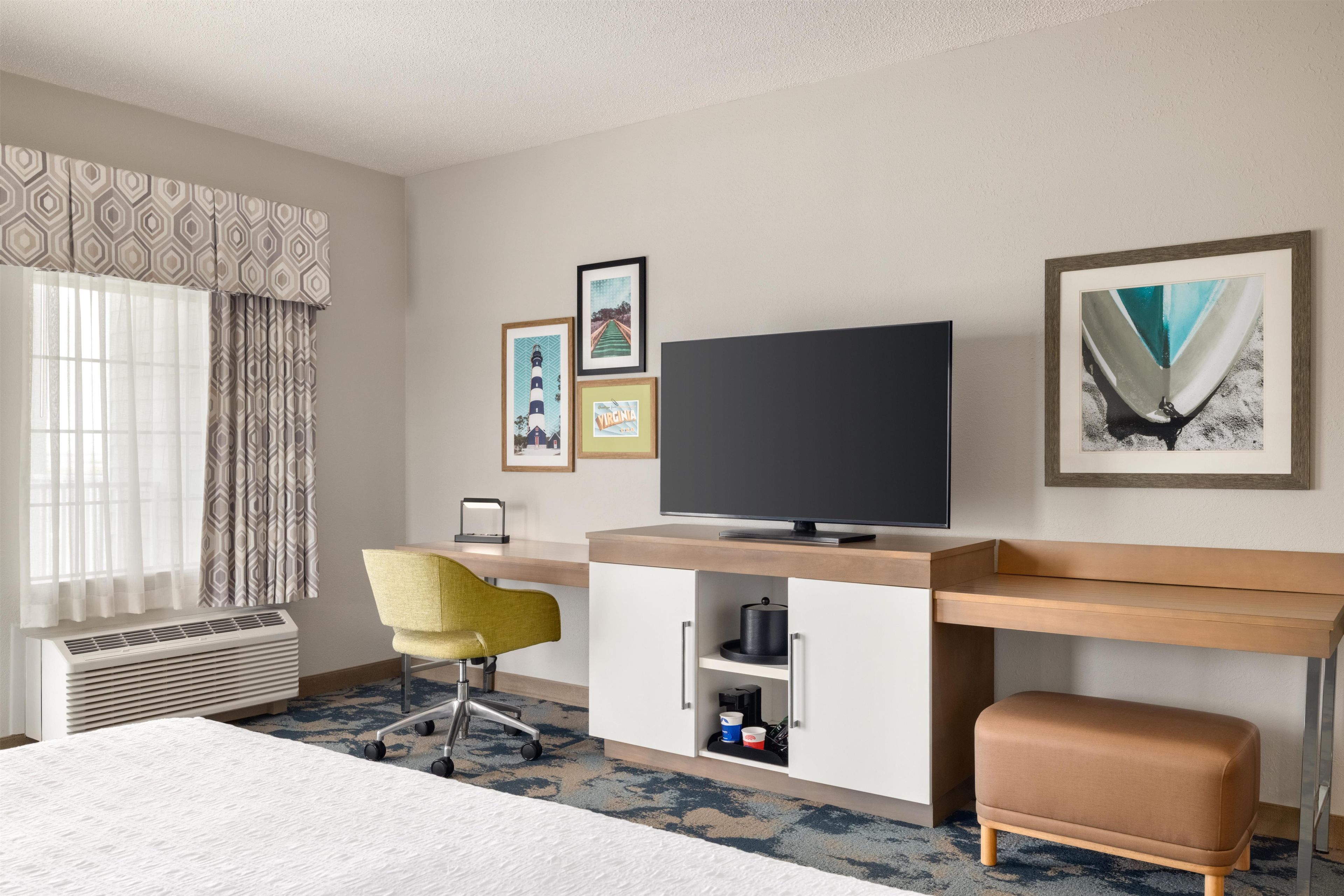 Een hotelkamer met een bed, een bureau met een computer, een stoel, een televisie en ingekaderde foto's aan de muur.