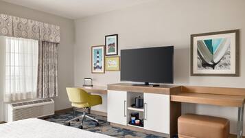 Een hotelkamer met een bed, een bureau met een computer, een stoel, een televisie en ingekaderde foto's aan de muur.