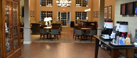 A hotel lobby with a chandelier, wooden furniture, and a coffee station.