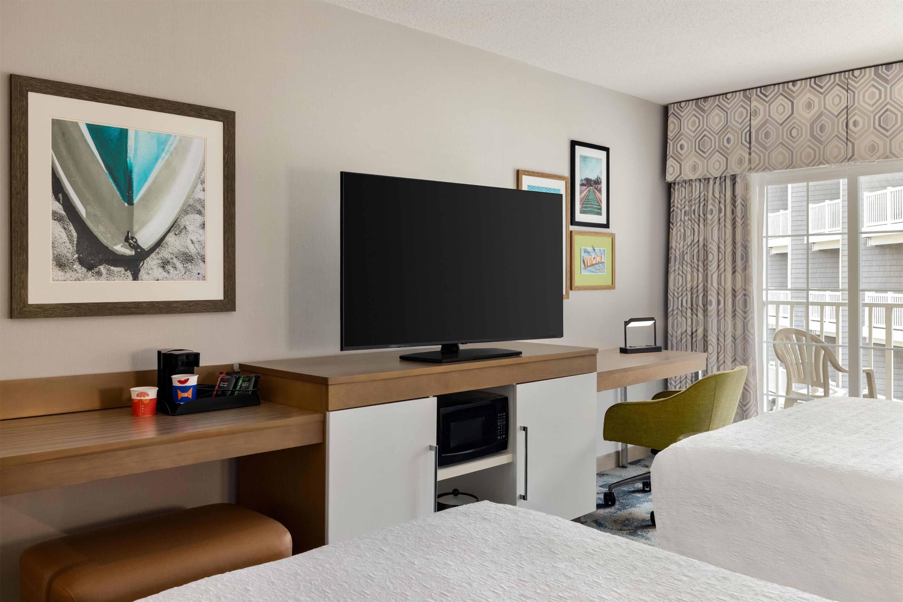Une chambre d’hôtel avec un téléviseur posé sur un meuble en bois, une machine à café et un lit recouvert d’une couverture blanche à texture.