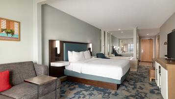 A hotel room with a bed, a desk, a chair, a TV, and a bathroom visible in the background.