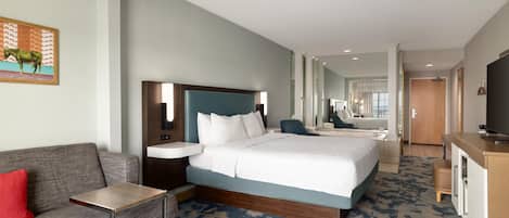 A hotel room with a bed, a desk, a chair, a TV, and a bathroom visible in the background.