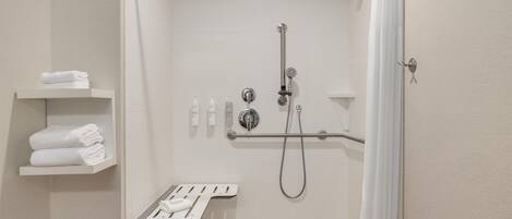 Un espace douche moderne doté d’un pommeau de douche à main, d’un flexible de douche et d’un robinet mural. Trois serviettes blanches sont pliées et empilées sur une étagère située à gauche.