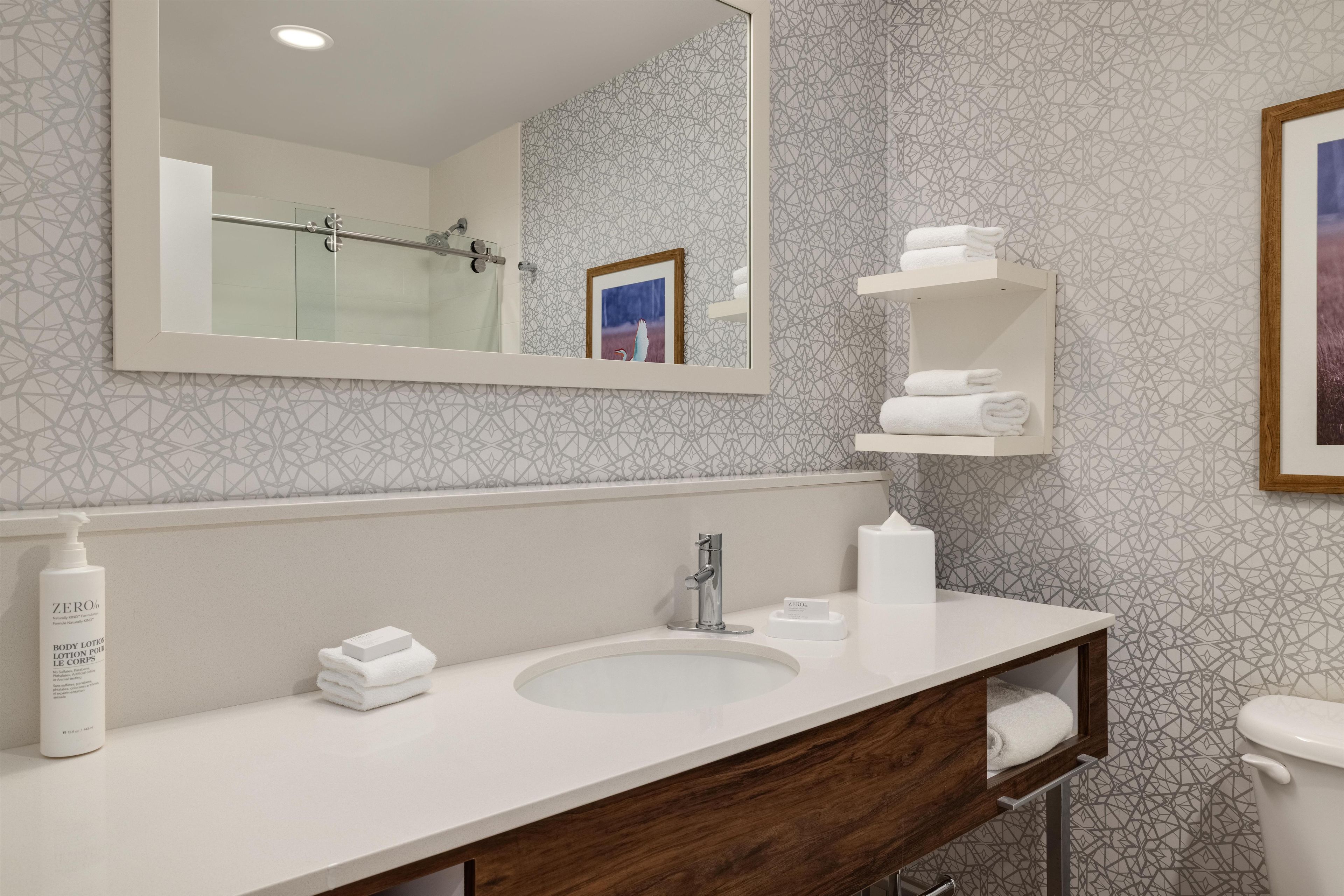 A modern bathroom with a large mirror, a sink, a toilet, and a shower.
