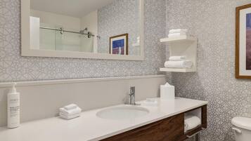 A modern bathroom with a large mirror, a sink, a toilet, and a shower.