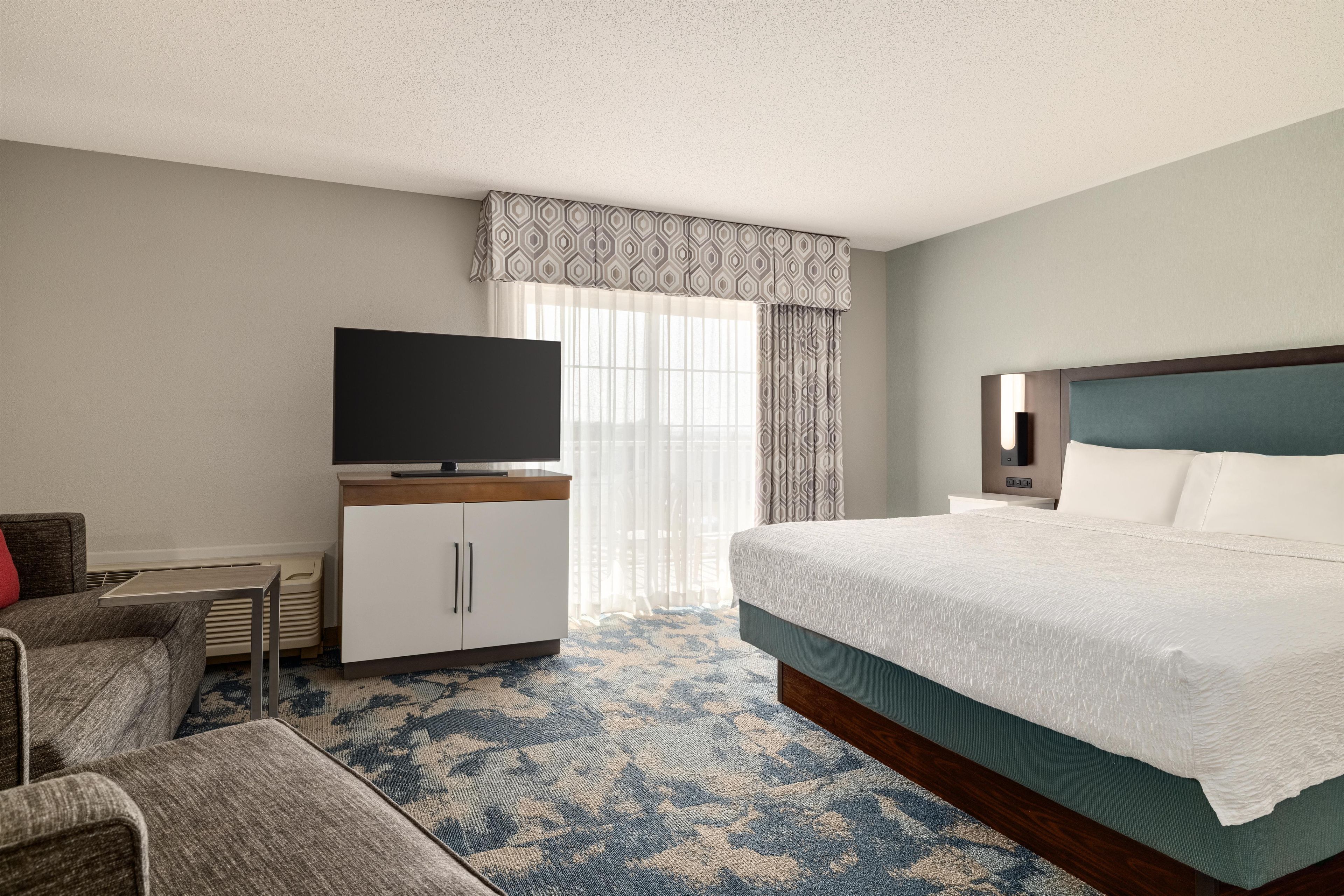 Una habitación de hotel con una cama, un televisor sobre un mueble, un escritorio y una silla.