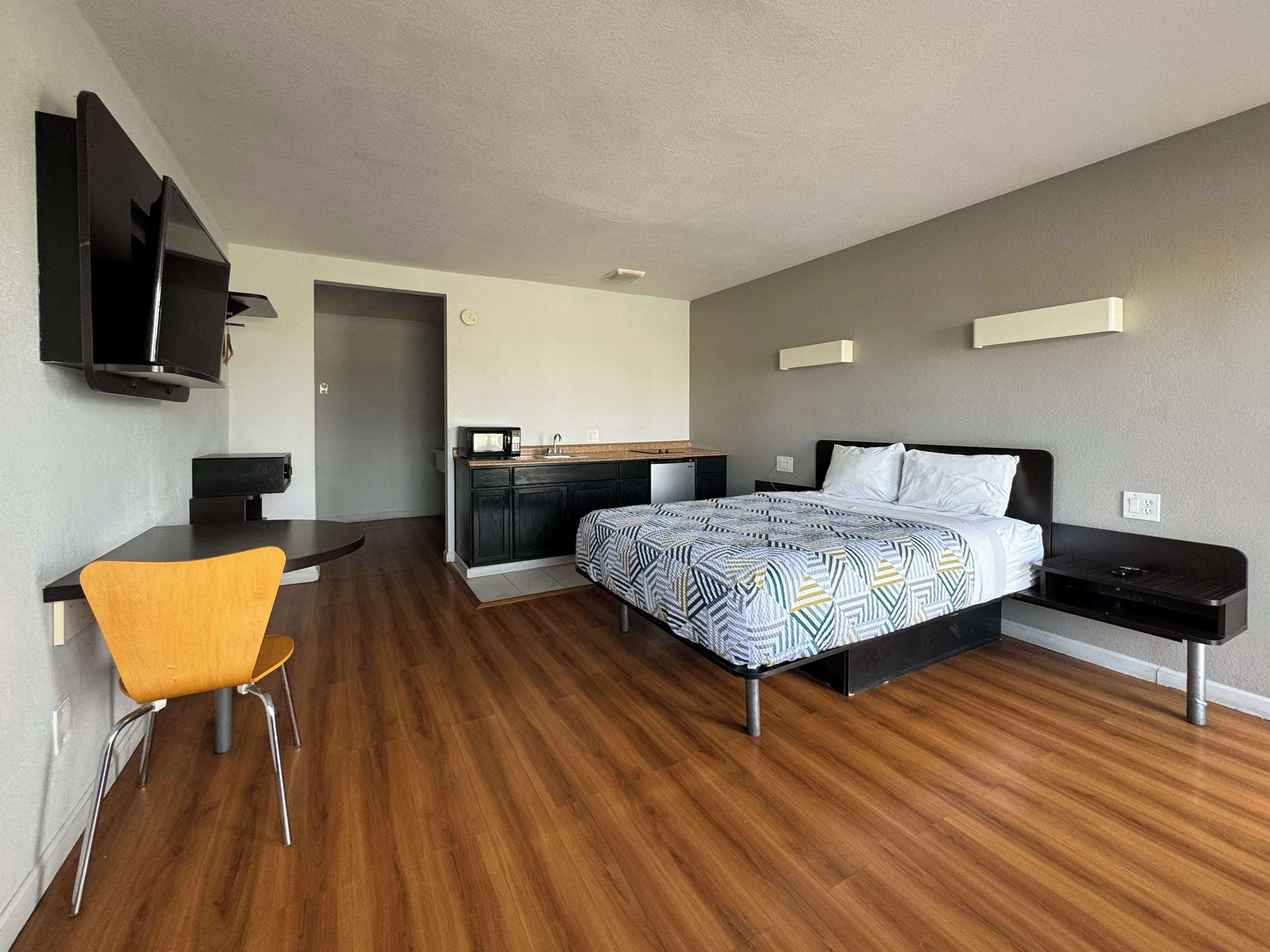 Ein modernes Hotelzimmer mit einem Bett, einem Schreibtisch, einem Sessel, einer Mikrowelle und einem Fernseher.