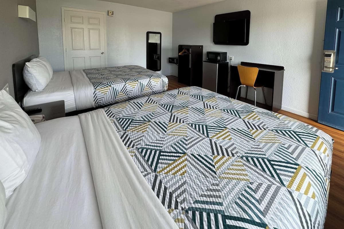 Une chambre d’hôtel avec deux lits, un bureau, une chaise, une télévision et une armoire.