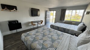 Une chambre d’hôtel avec deux lits, un bureau avec une chaise, une télévision et une fenêtre donnant sur des palmiers.