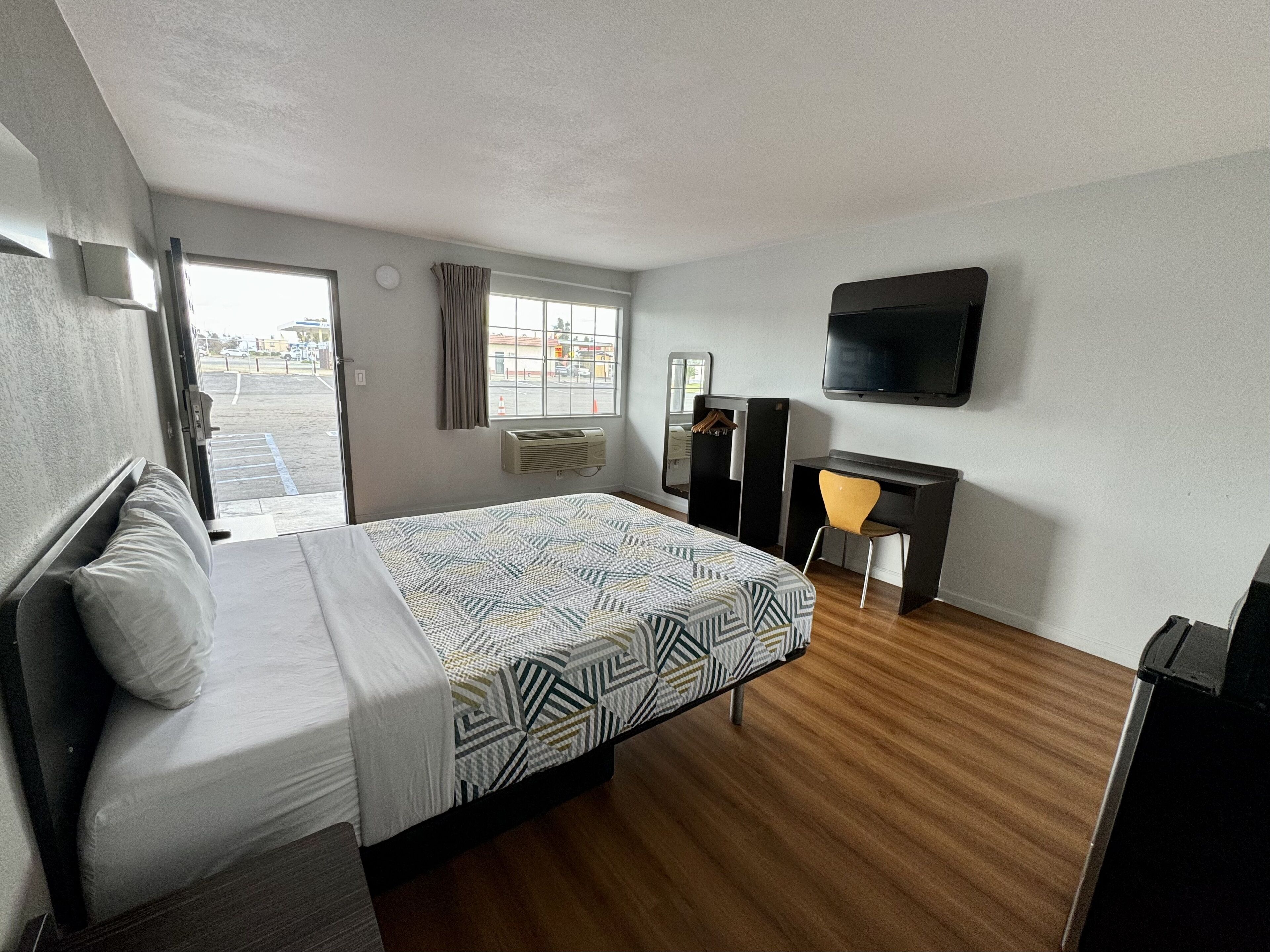 Habitación de hotel con cama, escritorio, silla, televisor y ventana con cortinas.