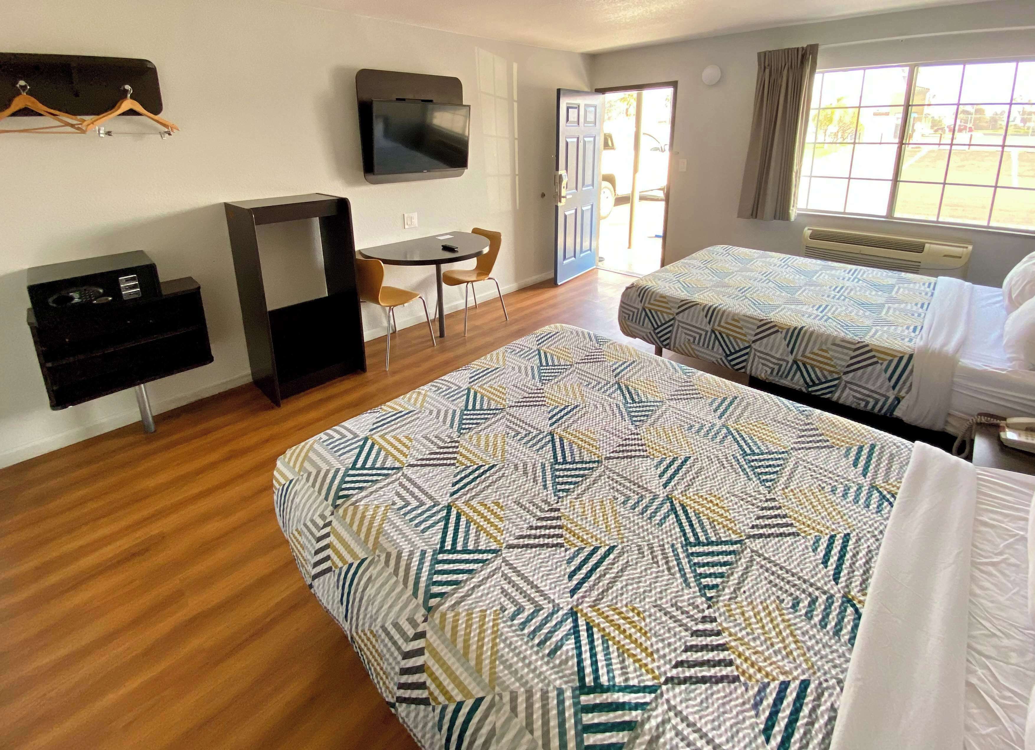 A hotel room with two beds, a TV mounted on the wall, a desk with a chair, and a window with curtains.