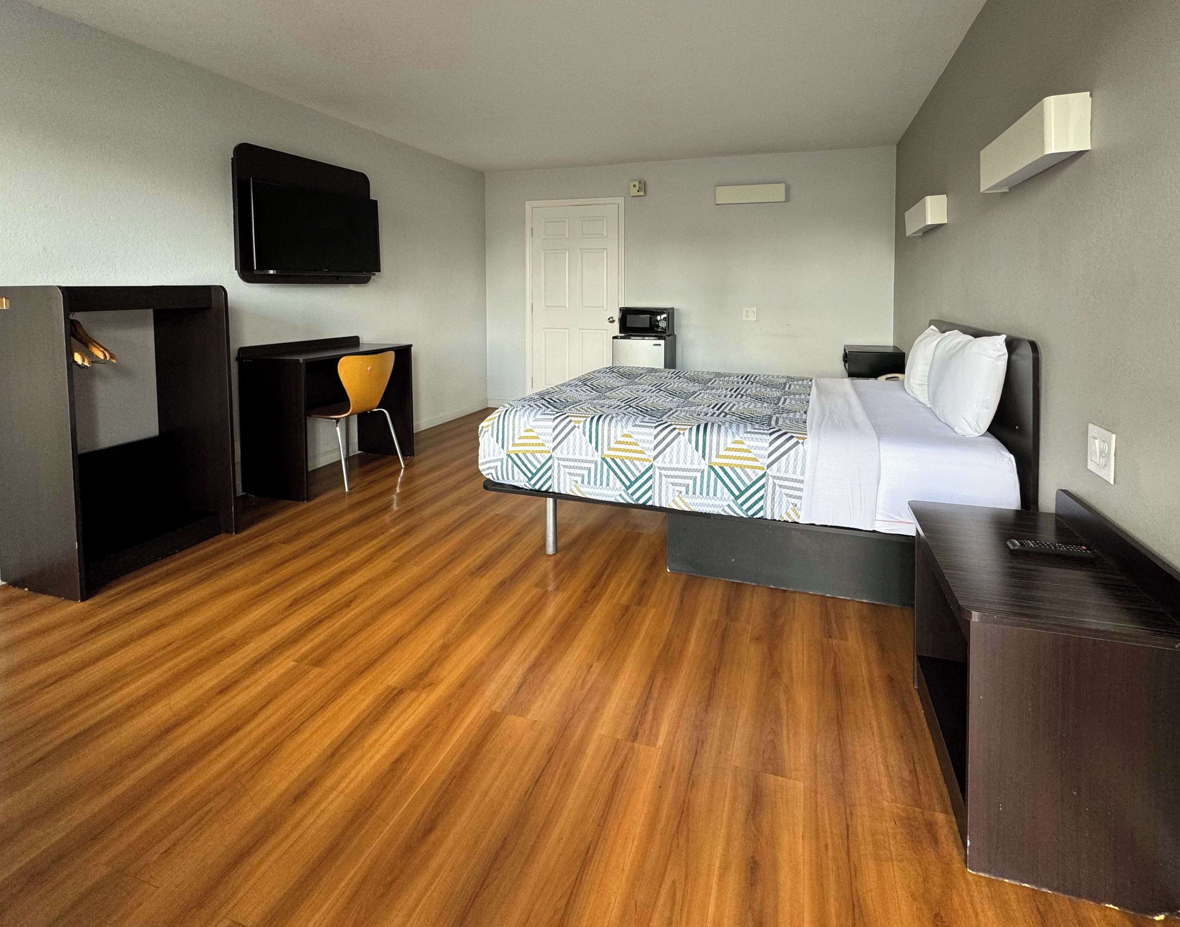 A hotel room with a bed, a desk, a chair, a television, and a door.