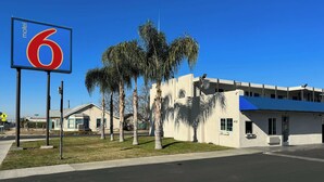 Un motel avec un grand panneau portant le chiffre « 6 », des palmiers et un bâtiment doté d’un toit bleu.