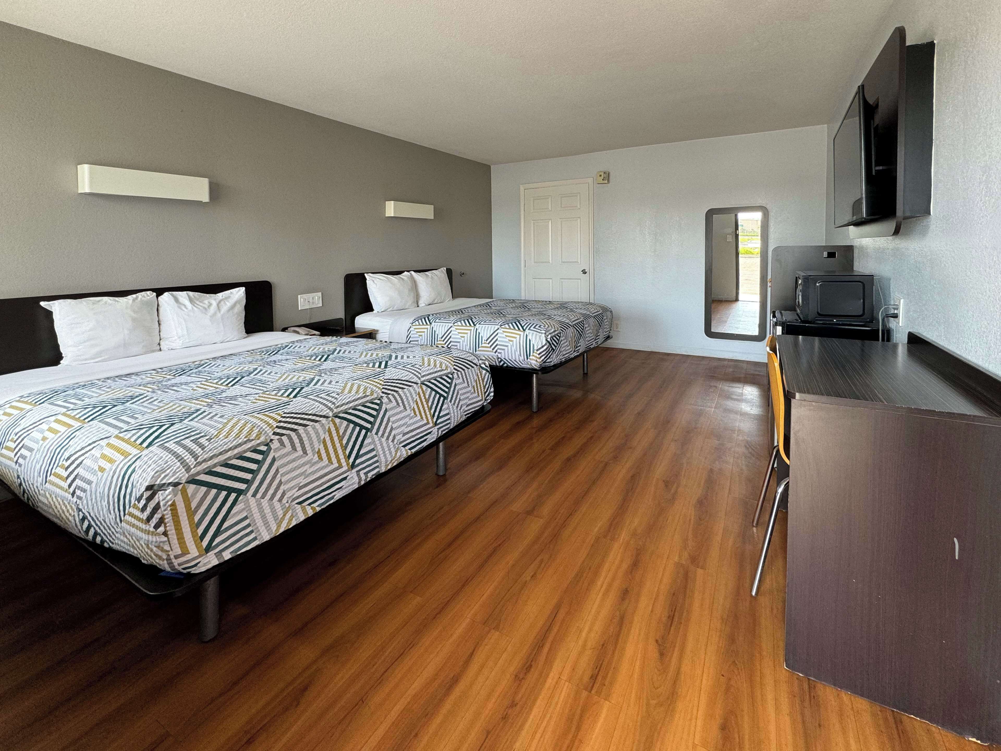 A hotel room with two beds, a wooden floor, a flat-screen TV, and a door leading to a balcony.