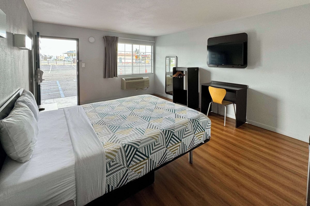 Une chambre d’hôtel avec un lit, un bureau, une chaise, une télévision et une fenêtre avec des rideaux.