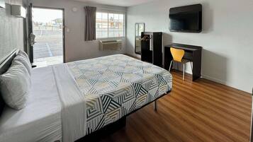 Quarto de hotel com cama, escrivaninha, cadeira, televisão e janela com cortinas.