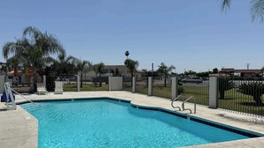 Une piscine rectangulaire, agréée pour la baignade mais interdisant les plongeons, entourée d’une terrasse en béton et d’une clôture métallique.