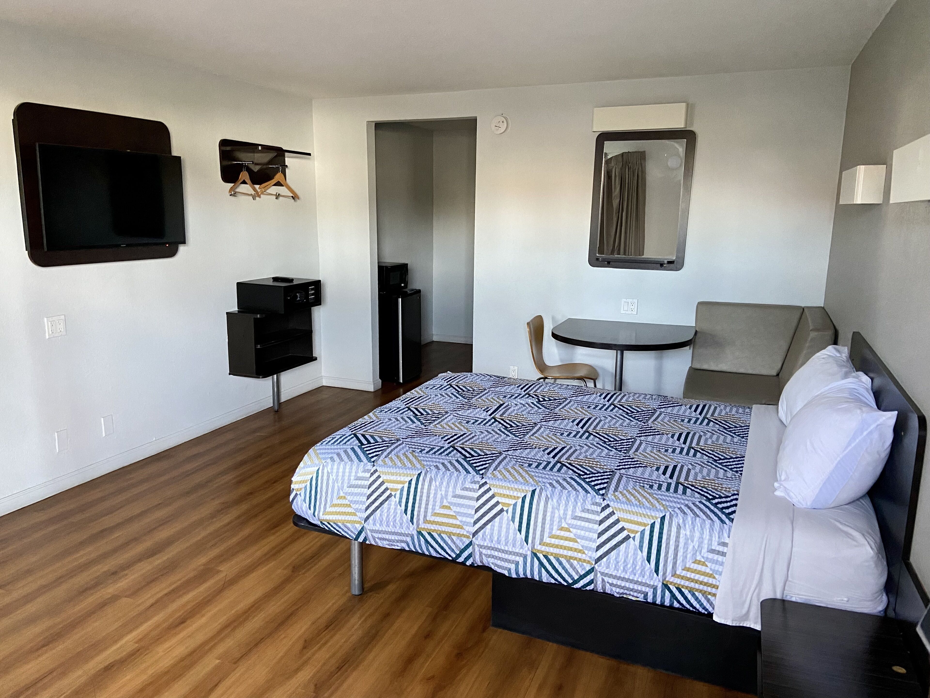A hotel room with a bed, a desk, a chair, a TV, and a small kitchenette.
