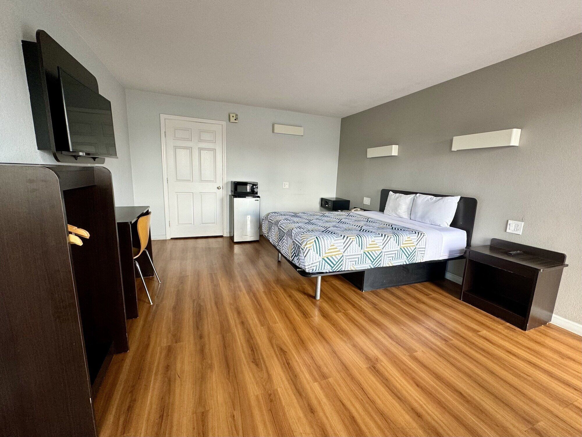 A hotel room with a bed, a desk, a chair, a TV, and a microwave.