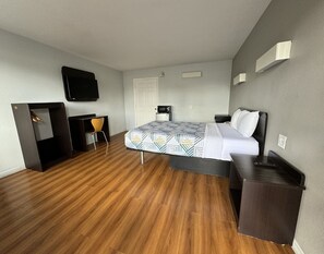 A hotel room with a bed, a desk, a chair, a television, and a microwave.