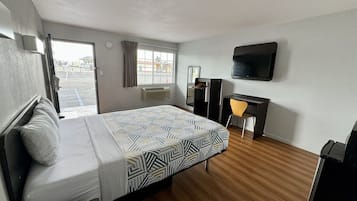 Una habitación de hotel con cama, escritorio, silla, televisor y ventana con cortinas.
